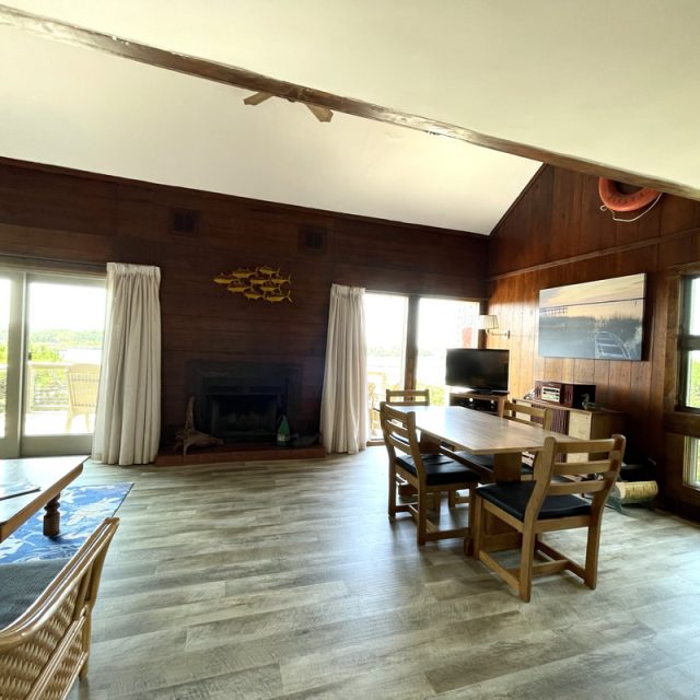 Spacious living and dining area with wood walls, large windows, light wood floors, and a fireplace.