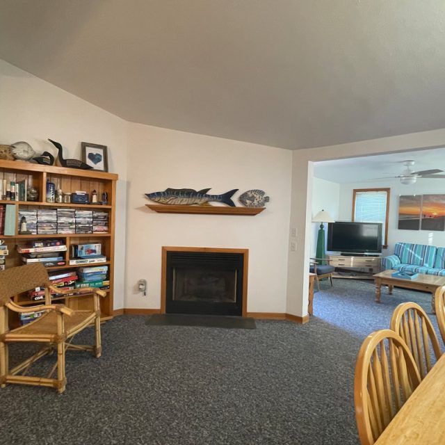 Living room with a wooden bookshelf, fireplace, wall art, and a view into a sitting area with striped furniture and TV.