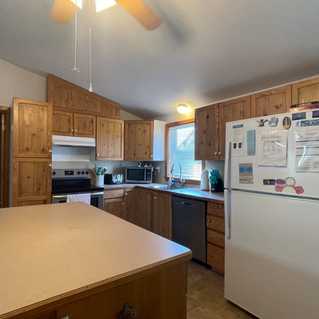 Kitchen with wooden cabinets, white appliances, an island countertop, and a window letting in natural light.