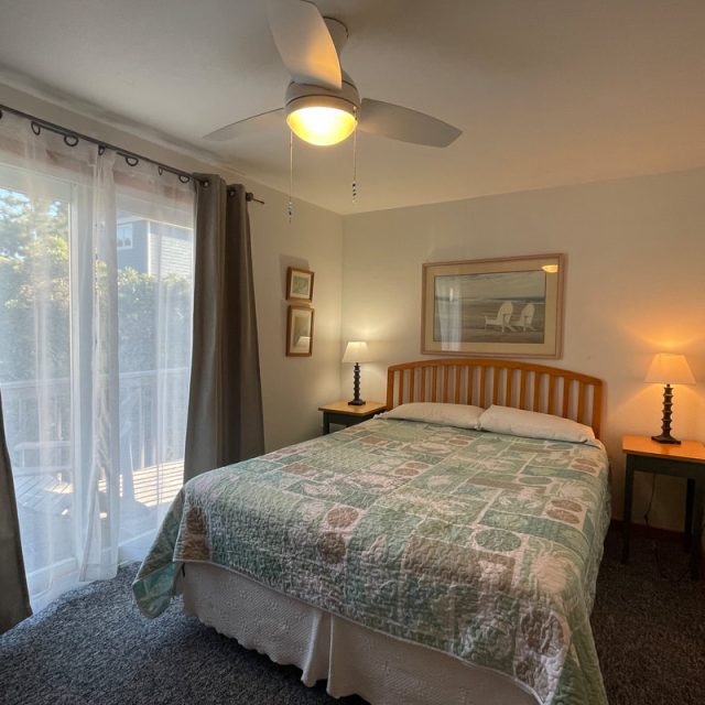 Bedroom with a double bed, two bedside tables with lamps, a ceiling fan, and large window with curtains.