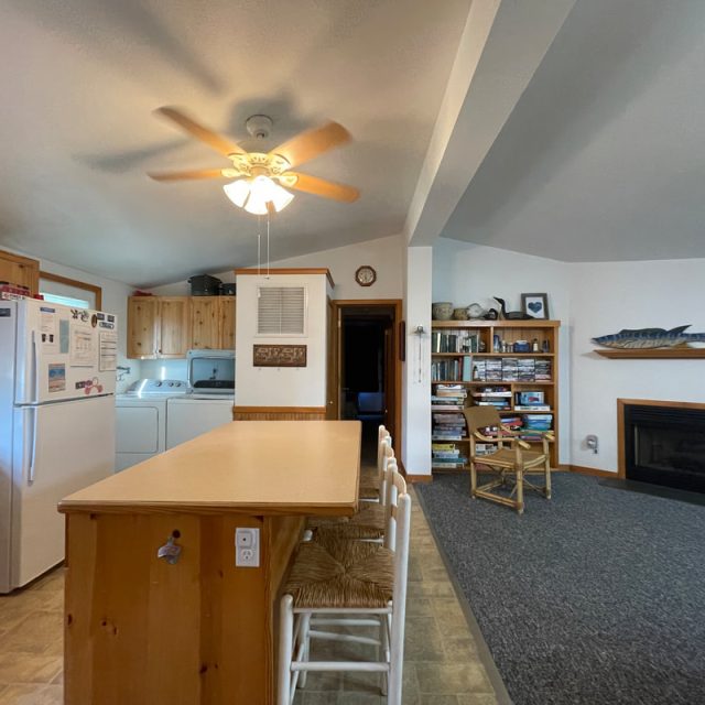 Kitchen and living area with wooden cabinets, island, washer-dryer, bookshelves, fireplace, and ceiling fan.