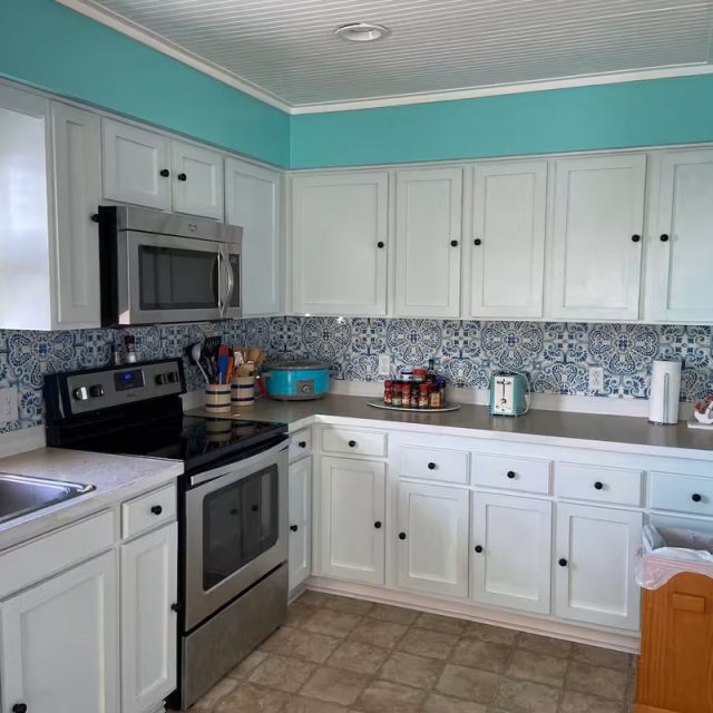 Kitchen with white cabinets, blue walls, patterned backsplash, stainless appliances, and various countertop items.