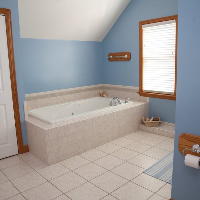 Bathroom with a large bathtub, blue walls, tiled floor, window with blinds, and a wall-mounted toilet paper holder.