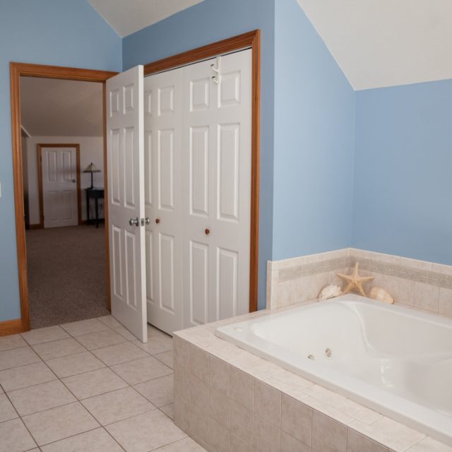Bathroom with a large bathtub, tiled floor, double doors, light wood cabinets, and blue walls.