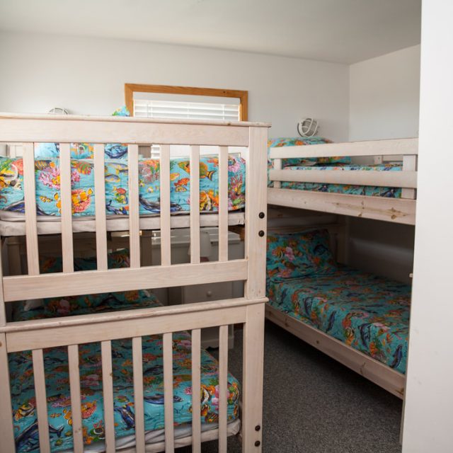 Small bedroom with two sets of light wood bunk beds, each with colorful floral bedding, and a window on the left.