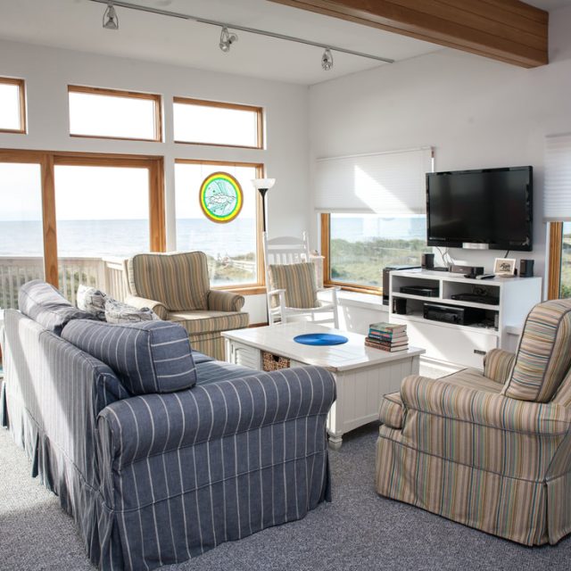 Living room with striped couches, a TV, and ocean view through large windows and a glass door.