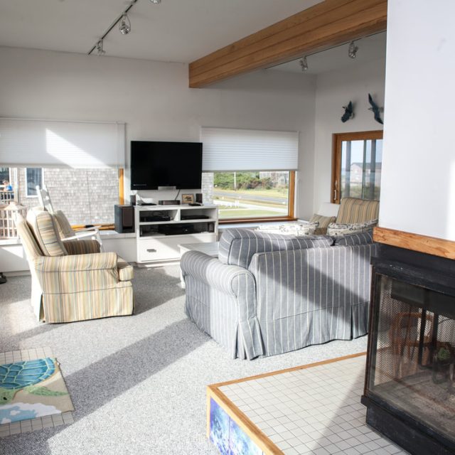 Bright living room with striped armchairs, a blue sofa, TV, large windows, and a fireplace in the foreground.