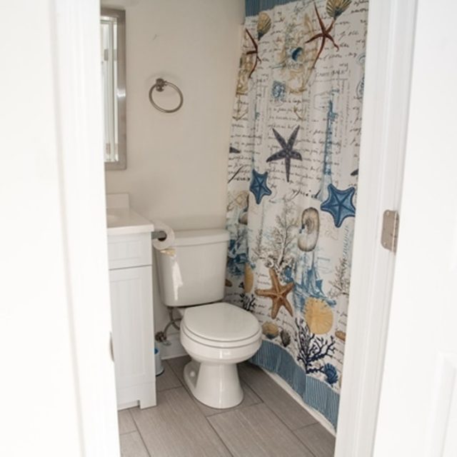 Small bathroom with white toilet, sink, and a shower curtain featuring a nautical and sea life pattern.